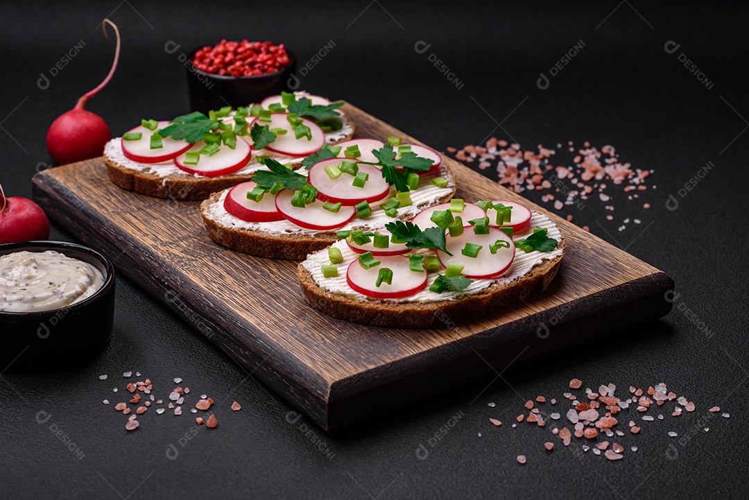 Delicioso sanduíche ou bruscheta com rabanete de cream cheese e cebolinha sobre um fundo escuro de concreto