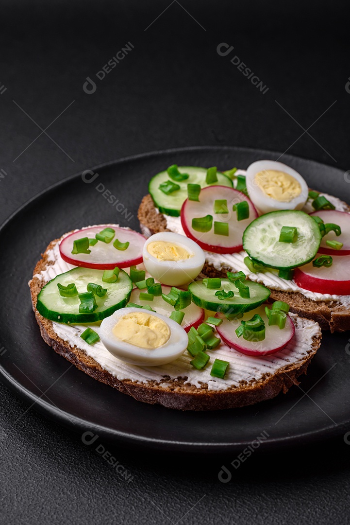 Delicioso sanduíche ou bruscheta com rabanete de cream cheese e cebolinha sobre um fundo escuro de concreto