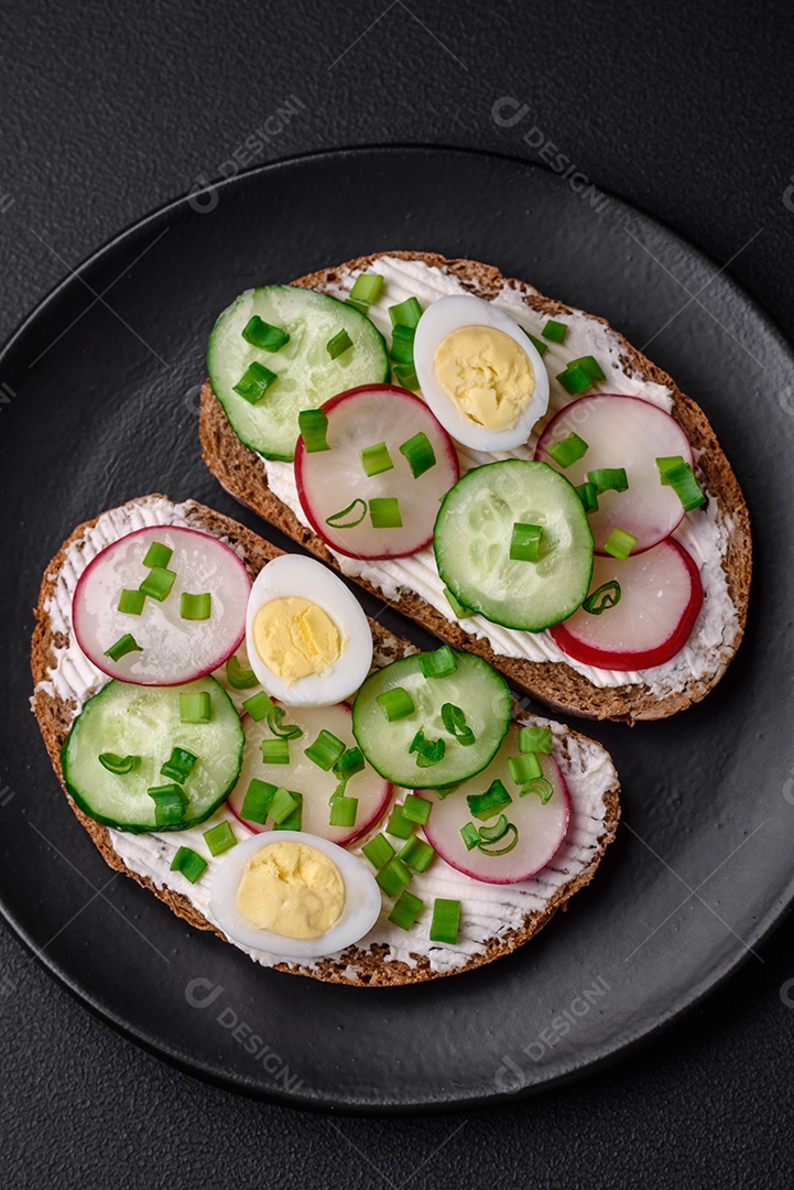 Delicioso sanduíche ou bruscheta com rabanete de cream cheese e cebolinha sobre um fundo escuro de concreto