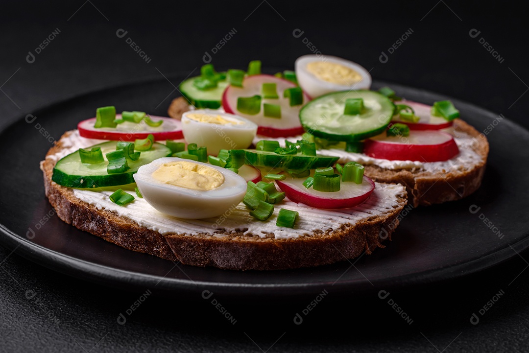 Delicioso sanduíche ou bruscheta com rabanete de cream cheese e cebolinha sobre um fundo escuro de concreto