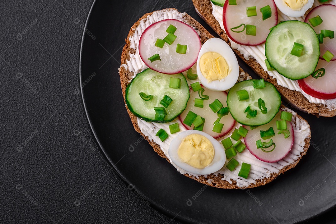 Delicioso sanduíche ou bruscheta com rabanete de cream cheese e cebolinha sobre um fundo escuro de concreto