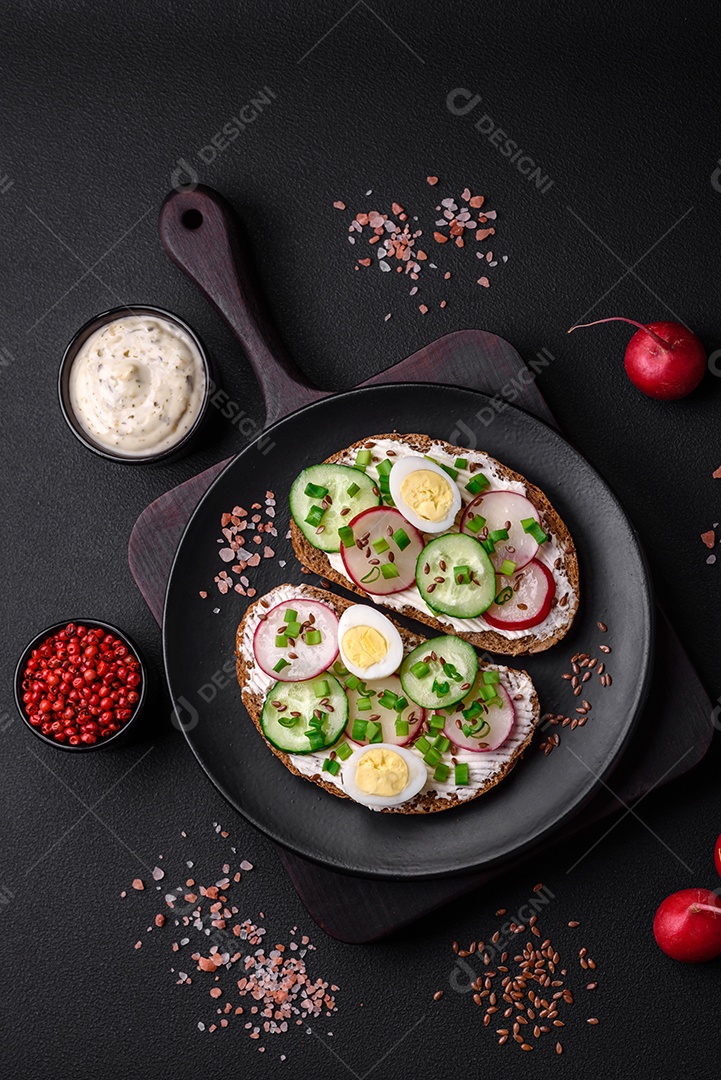 Delicioso sanduíche ou bruscheta com rabanete de cream cheese e cebolinha sobre um fundo escuro de concreto