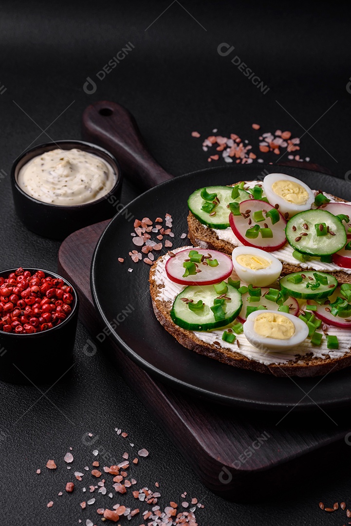 Delicioso sanduíche ou bruscheta com rabanete de cream cheese e cebolinha sobre um fundo escuro de concreto