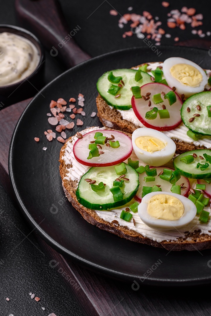 Delicioso sanduíche ou bruscheta com rabanete de cream cheese e cebolinha sobre um fundo escuro de concreto