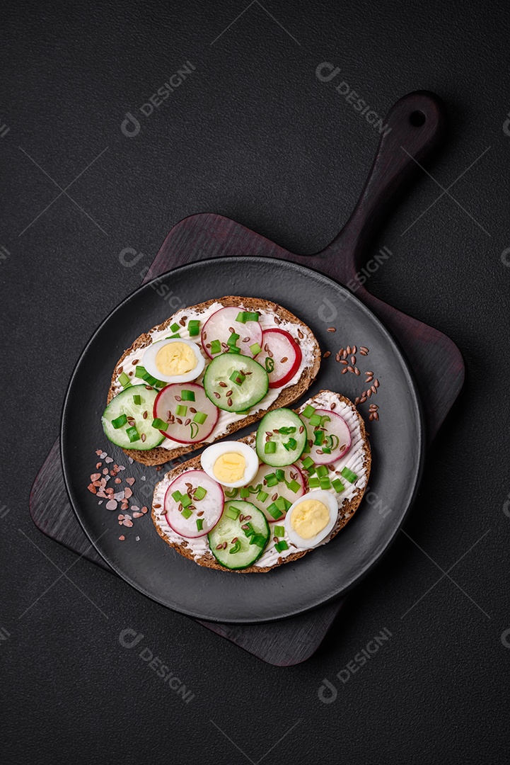 Delicioso sanduíche ou bruscheta com rabanete de cream cheese e cebolinha sobre um fundo escuro de concreto