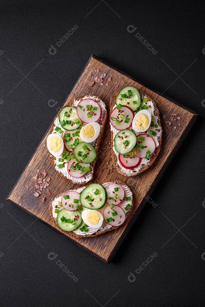 Delicioso sanduíche ou bruscheta com rabanete de cream cheese e cebolinha sobre um fundo escuro de concreto