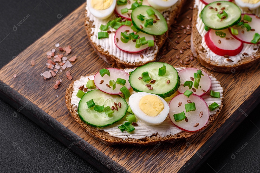 Delicioso sanduíche ou bruscheta com rabanete de cream cheese e cebolinha sobre um fundo escuro de concreto