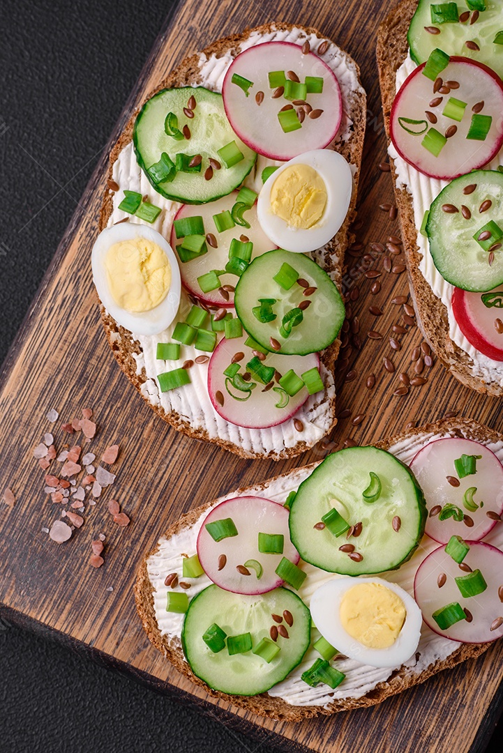 Delicioso sanduíche ou bruscheta com rabanete de cream cheese e cebolinha sobre um fundo escuro de concreto