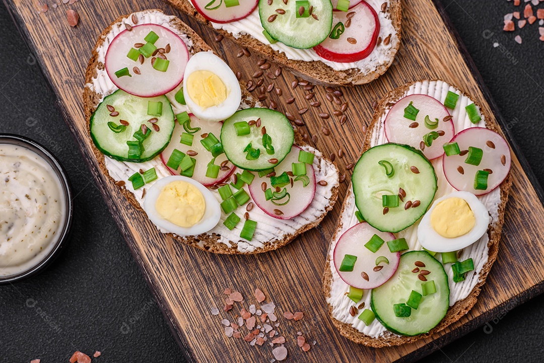 Delicioso sanduíche ou bruscheta com rabanete de cream cheese e cebolinha sobre um fundo escuro de concreto