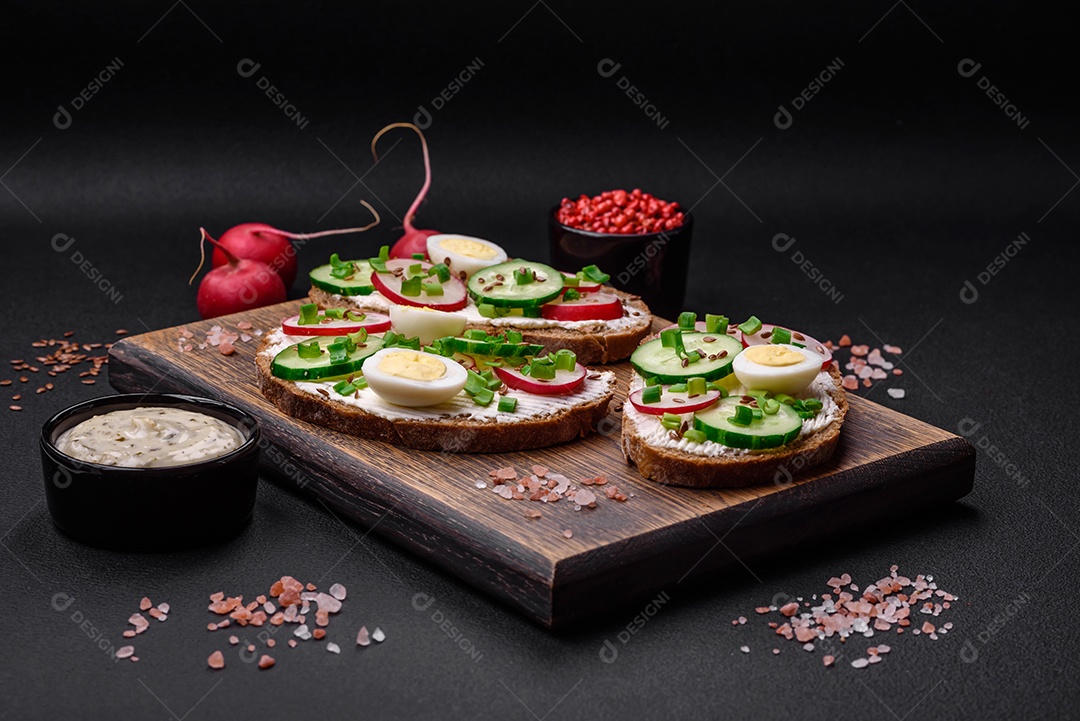 Delicioso sanduíche ou bruscheta com rabanete de cream cheese e cebolinha sobre um fundo escuro de concreto
