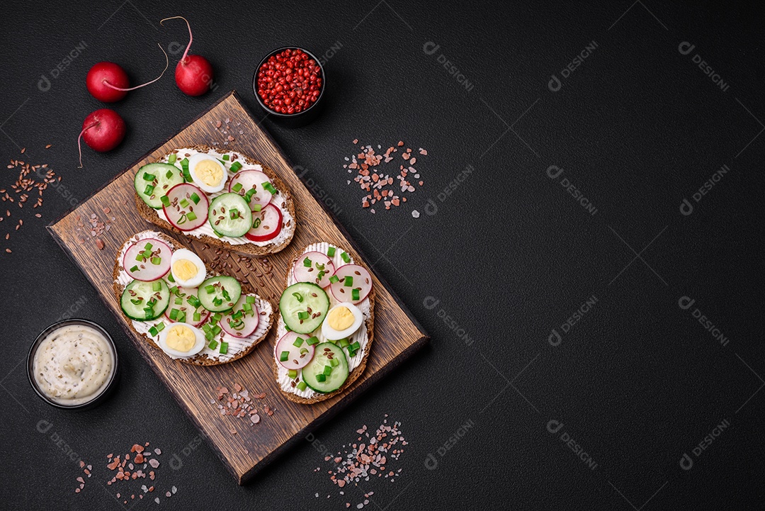 Delicioso sanduíche ou bruscheta com rabanete de cream cheese e cebolinha sobre um fundo escuro de concreto