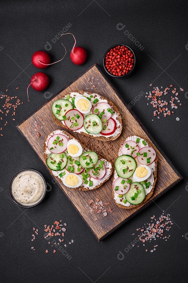 Delicioso sanduíche ou bruscheta com rabanete de cream cheese e cebolinha sobre um fundo escuro de concreto