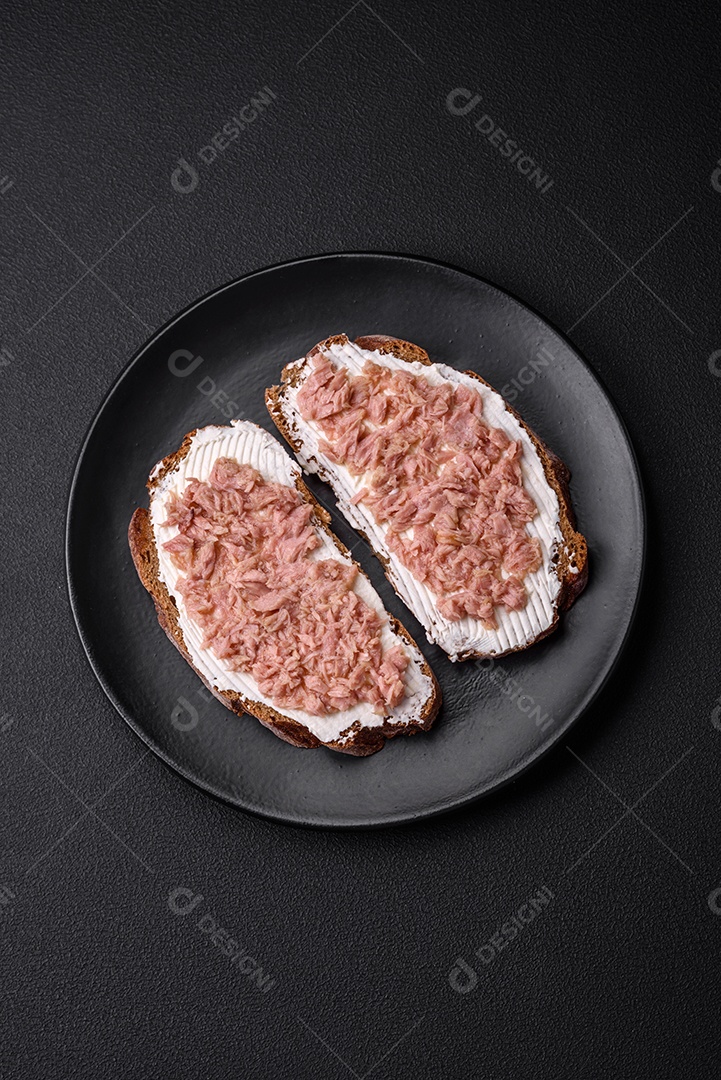 Deliciosos sanduíches compostos por torradas grelhadas, atum enlatado e cream cheese sobre um fundo escuro de concreto