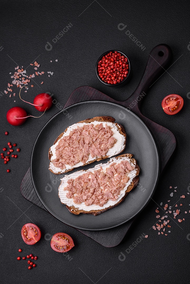 Deliciosos sanduíches compostos por torradas grelhadas, atum enlatado e cream cheese sobre um fundo escuro de concreto