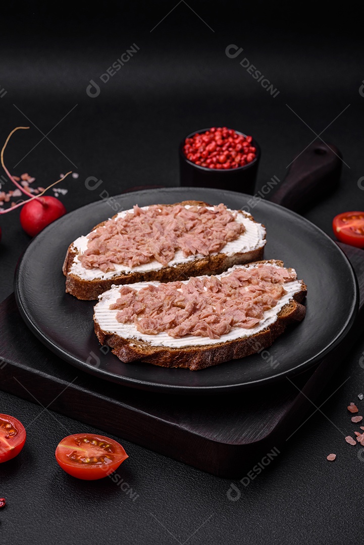 Deliciosos sanduíches compostos por torradas grelhadas, atum enlatado e cream cheese sobre um fundo escuro de concreto