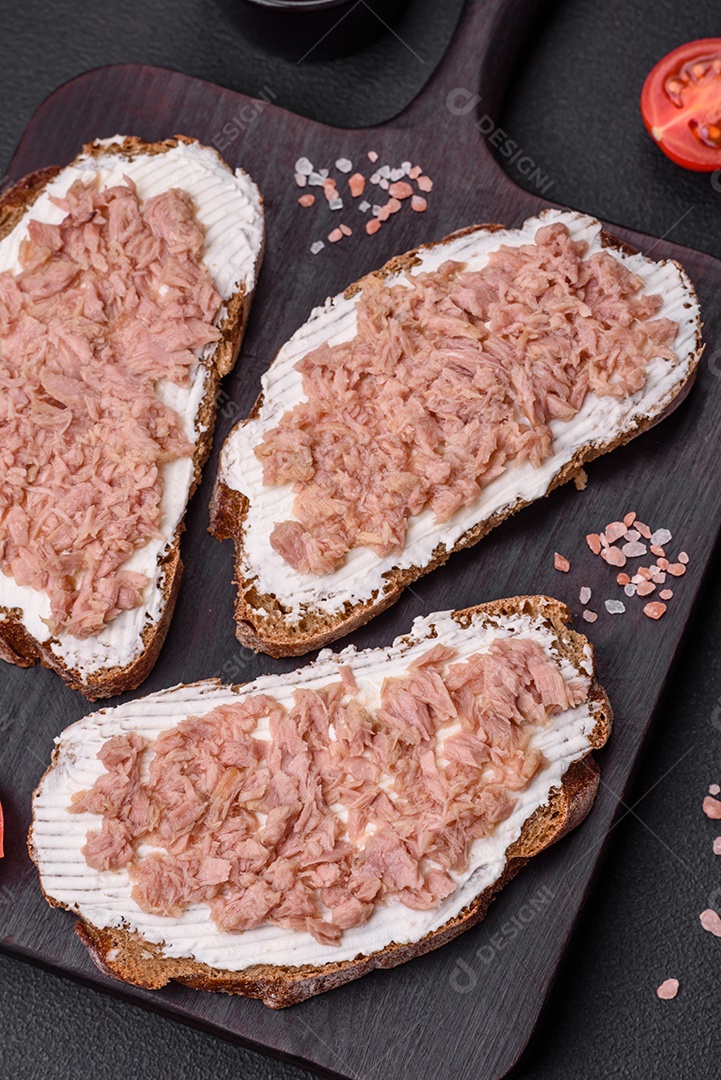 Deliciosos sanduíches compostos por torradas grelhadas, atum enlatado e cream cheese sobre um fundo escuro de concreto