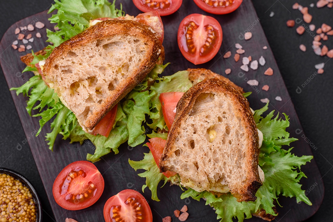 Delicioso sanduíche caprese com torradas grelhadas, mussarela, alface e tomate sobre fundo escuro de concreto