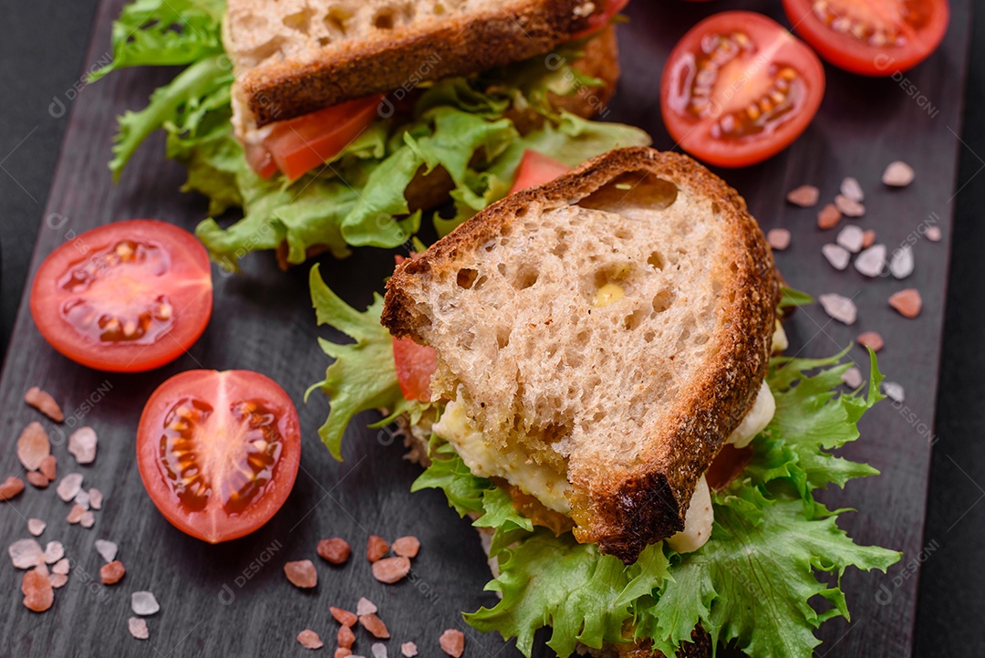 Delicioso sanduíche caprese com torradas grelhadas, mussarela, alface e tomate sobre fundo escuro de concreto