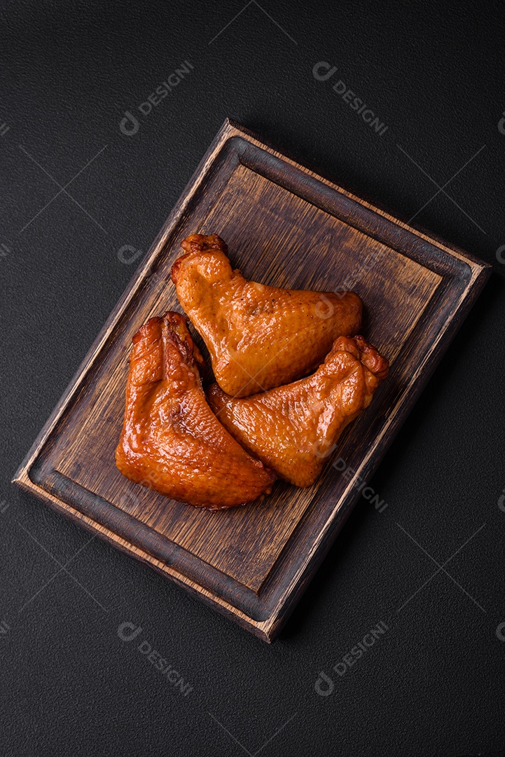 Deliciosas asas de frango grelhado com especiarias e ervas em um fundo escuro de concreto