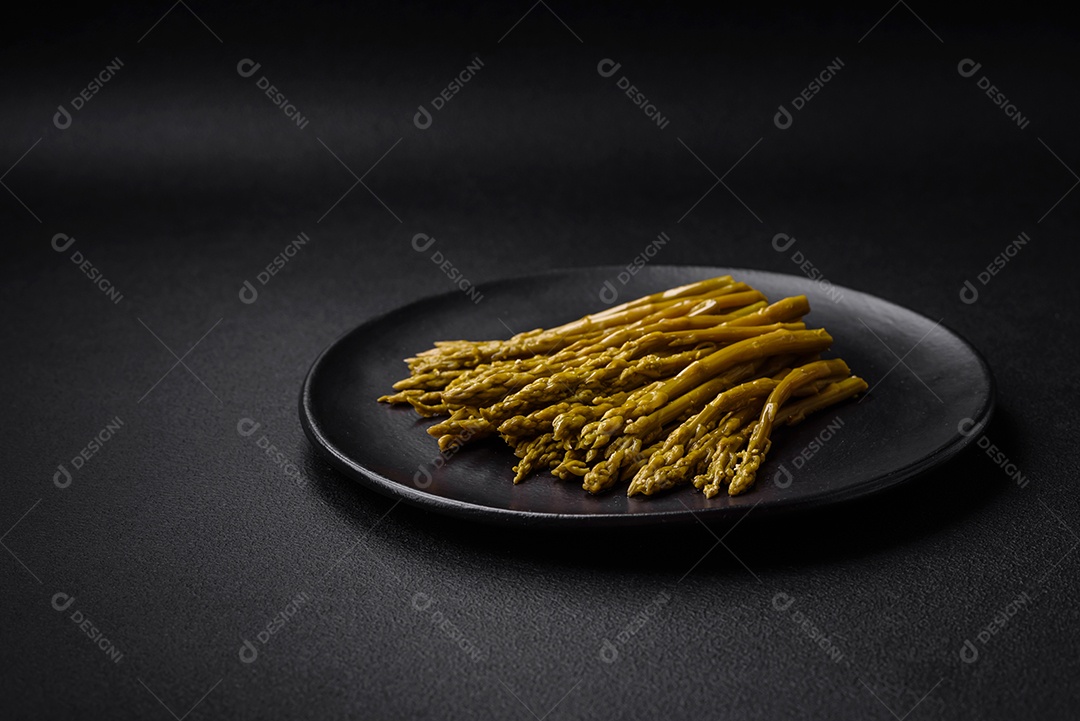 Raminhos de deliciosos espargos enlatados em uma placa de cerâmica preta sobre um fundo escuro de concreto