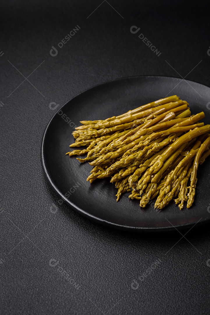 Raminhos de deliciosos espargos enlatados em uma placa de cerâmica preta sobre um fundo escuro de concreto