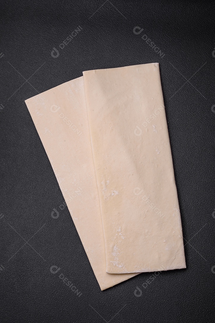 Folhas de massa folhada crua sobre um fundo escuro de concreto. Cozinhar pastéis doces em casa