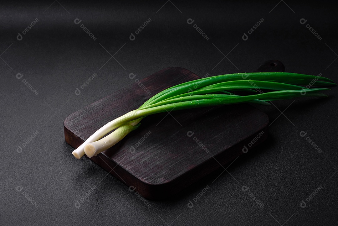 Cebolas verdes frescas sobre uma tábua retangular de madeira sobre um fundo escuro de concreto