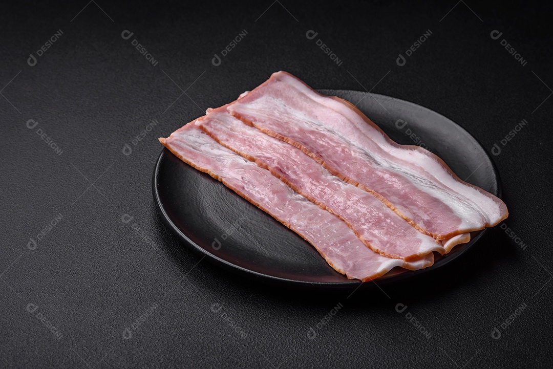 Deliciosas listras de bacon fresco com especiarias e sal sobre um fundo escuro de concreto