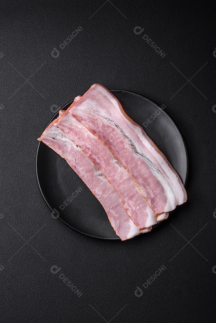 Deliciosas listras de bacon fresco com especiarias e sal sobre um fundo escuro de concreto