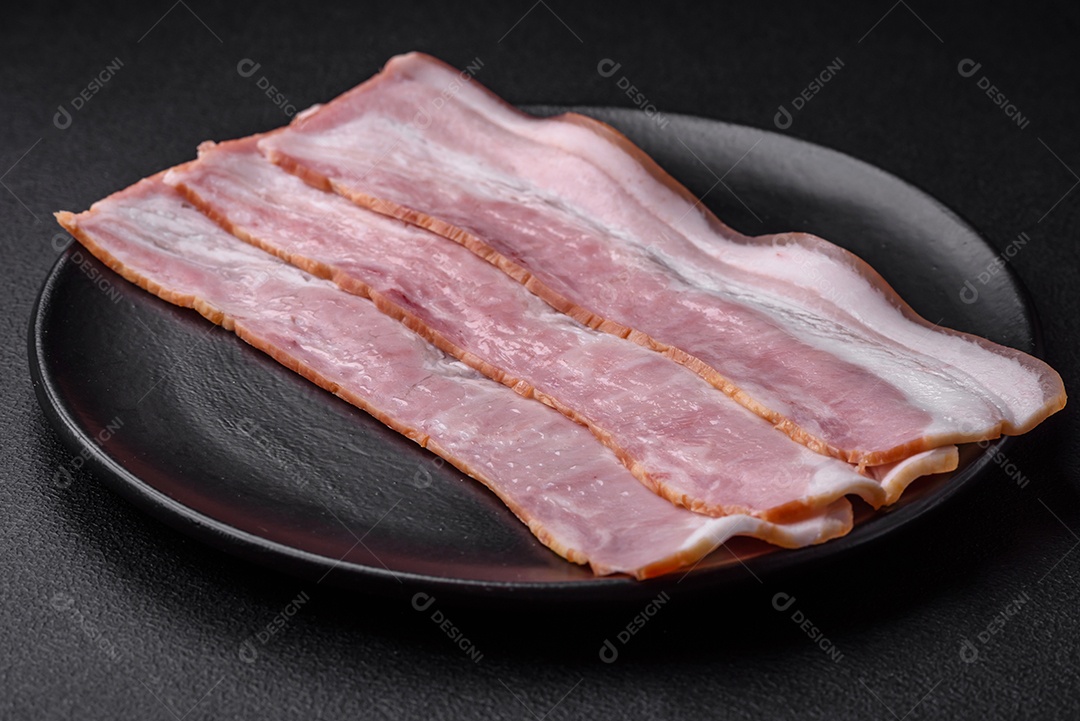 Deliciosas listras de bacon fresco com especiarias e sal sobre um fundo escuro de concreto