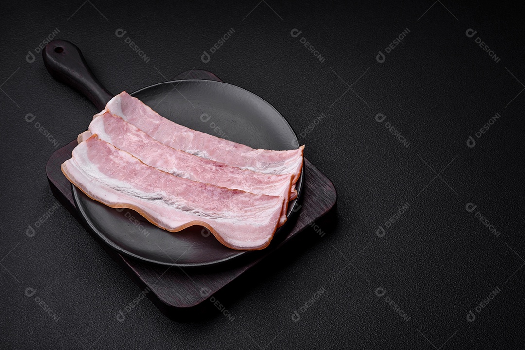 Deliciosas listras de bacon fresco com especiarias e sal sobre um fundo escuro de concreto