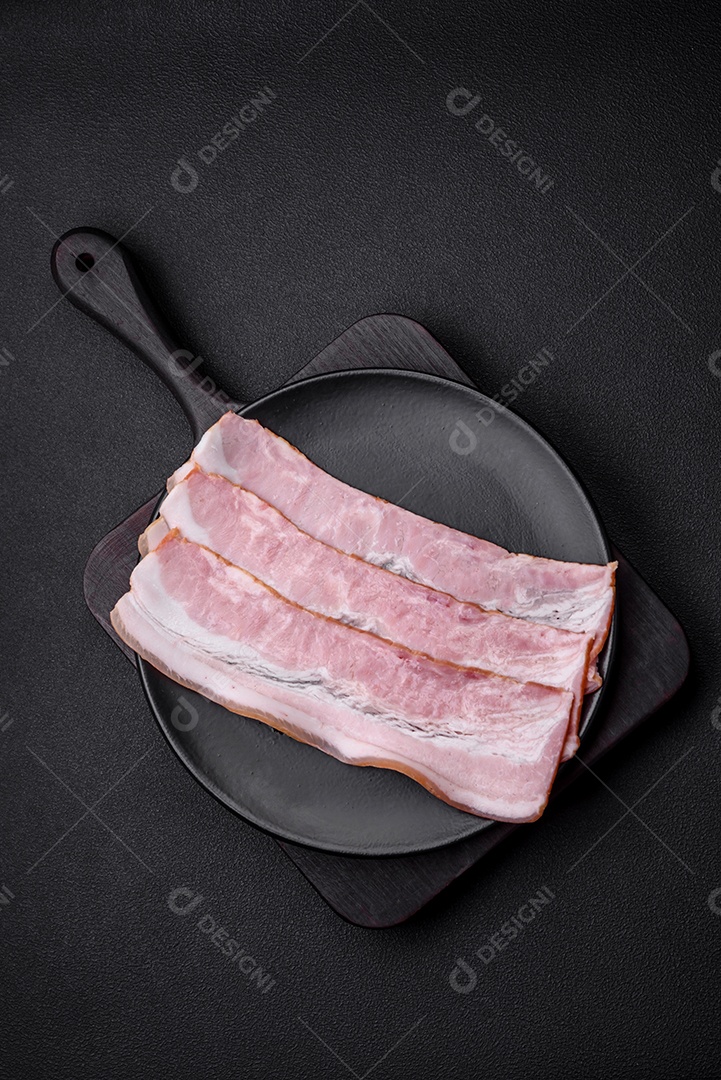 Deliciosas listras de bacon fresco com especiarias e sal sobre um fundo escuro de concreto