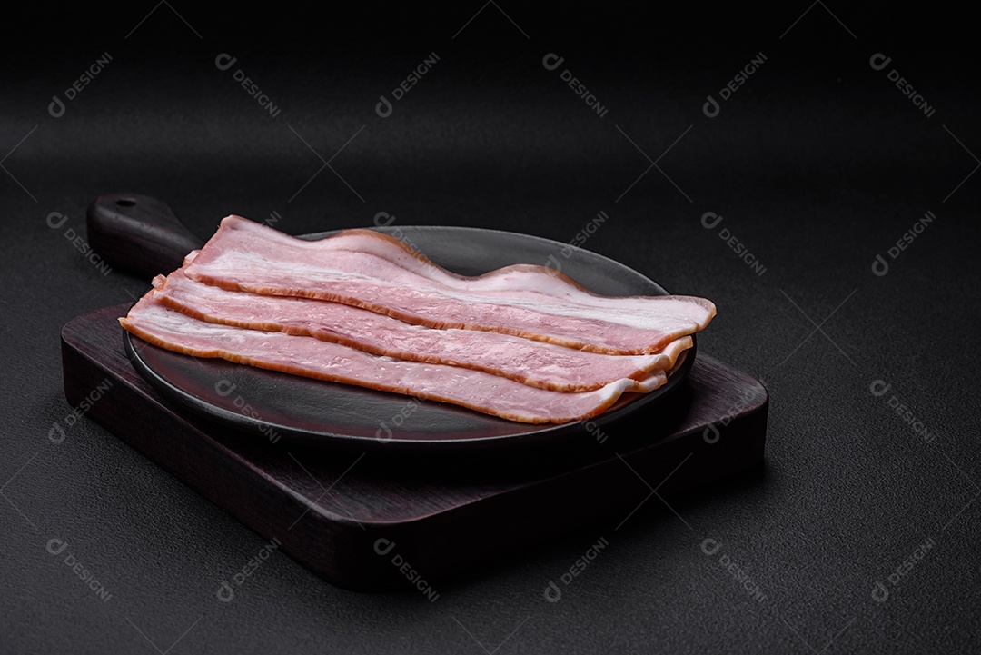 Deliciosas listras de bacon fresco com especiarias e sal sobre um fundo escuro de concreto