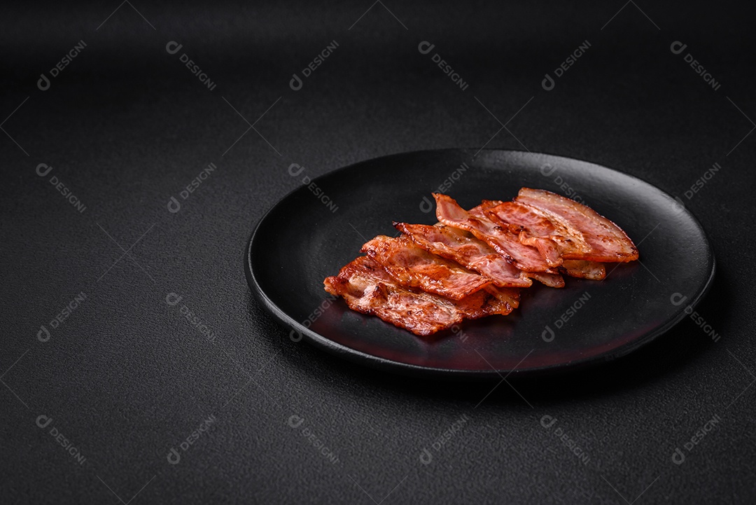 Deliciosas listras de bacon frito fresco com especiarias em um fundo escuro de concreto