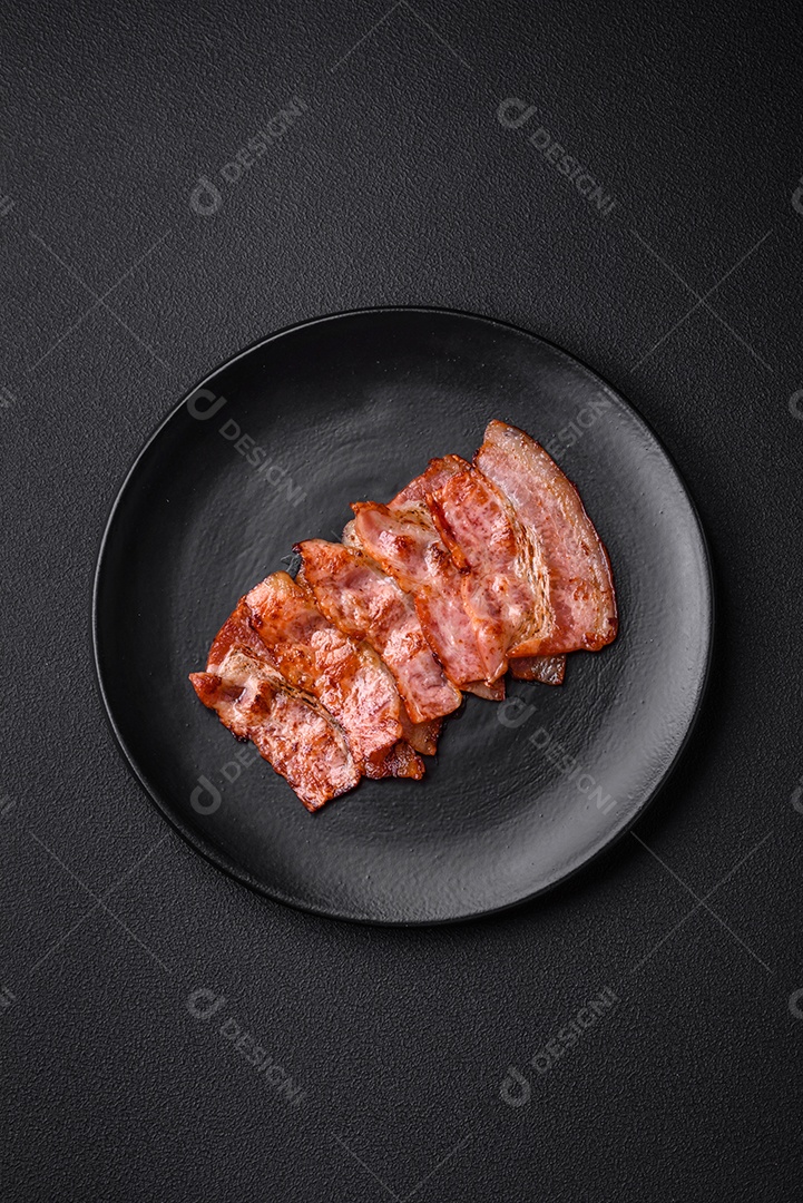 Deliciosas listras de bacon frito fresco com especiarias em um fundo escuro de concreto