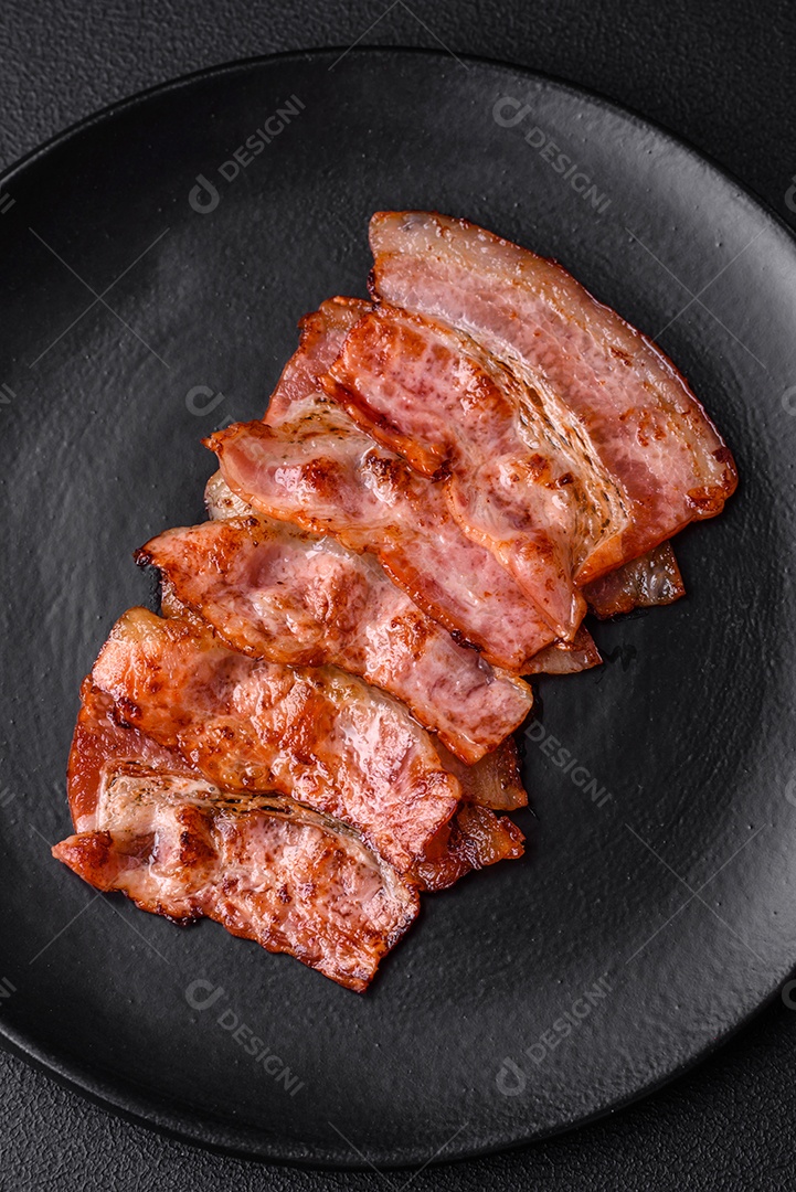 Deliciosas listras de bacon frito fresco com especiarias em um fundo escuro de concreto