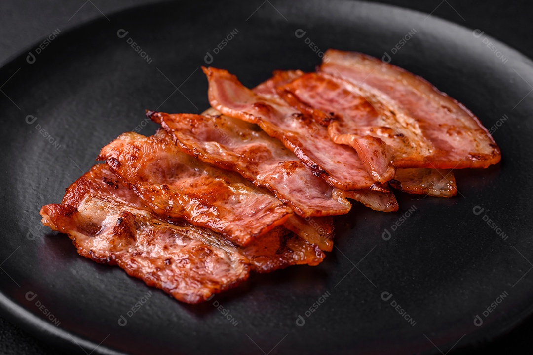 Deliciosas listras de bacon frito fresco com especiarias em um fundo escuro de concreto