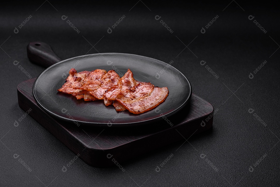 Deliciosas listras de bacon frito fresco com especiarias em um fundo escuro de concreto