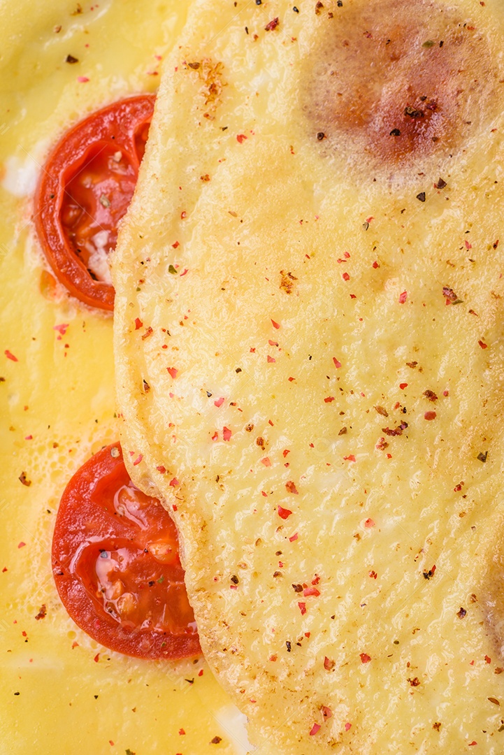 Deliciosa omelete fresca com tomate cereja, bacon, aspargos e especiarias sobre um fundo escuro de concreto