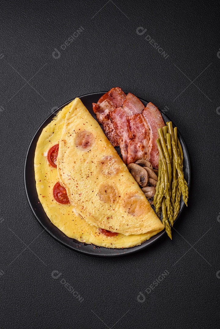 Deliciosa omelete fresca com tomate cereja, bacon, aspargos e especiarias sobre um fundo escuro de concreto