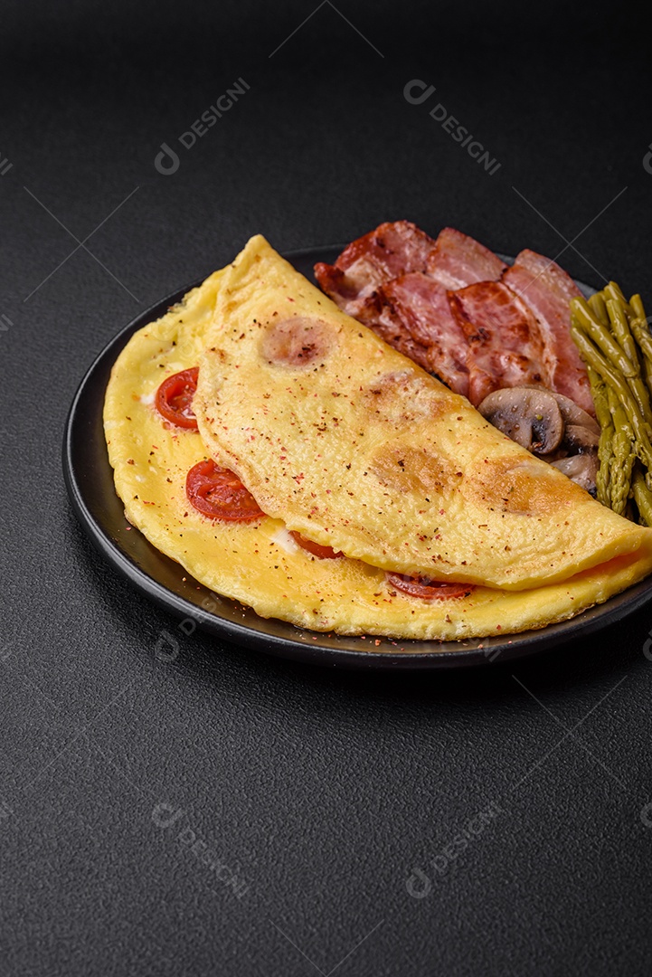Deliciosa omelete fresca com tomate cereja, bacon, aspargos e especiarias sobre um fundo escuro de concreto