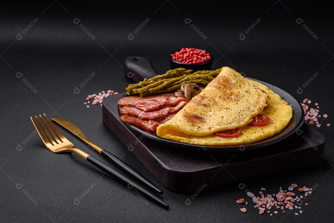 Deliciosa omelete fresca com tomate cereja, bacon, aspargos e especiarias sobre um fundo escuro de concreto