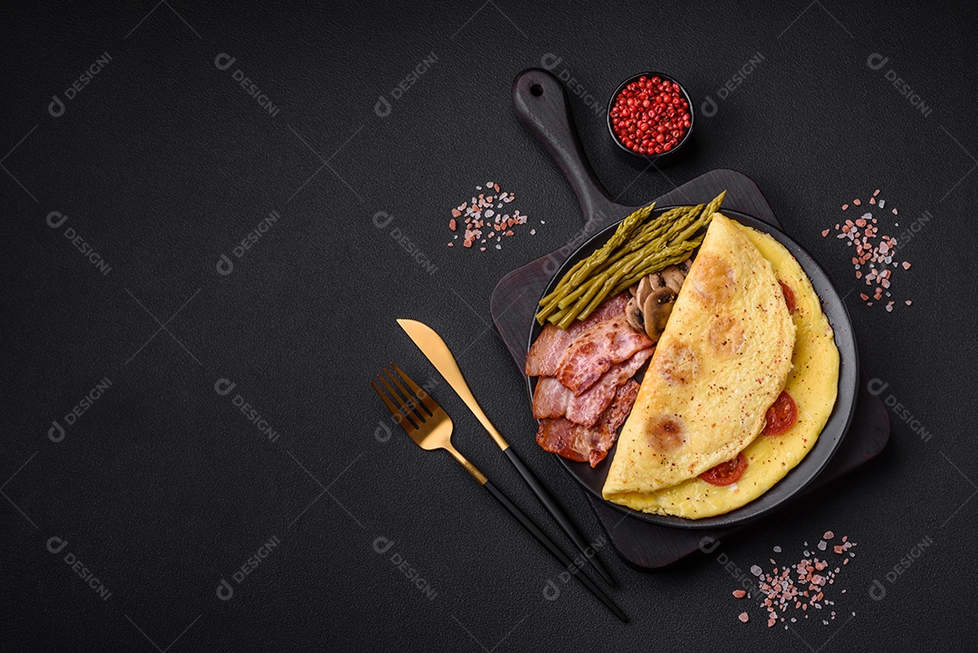 Deliciosa omelete fresca com tomate cereja, bacon, aspargos e especiarias sobre um fundo escuro de concreto