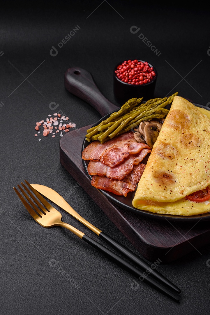 Deliciosa omelete fresca com tomate cereja, bacon, aspargos e especiarias sobre um fundo escuro de concreto