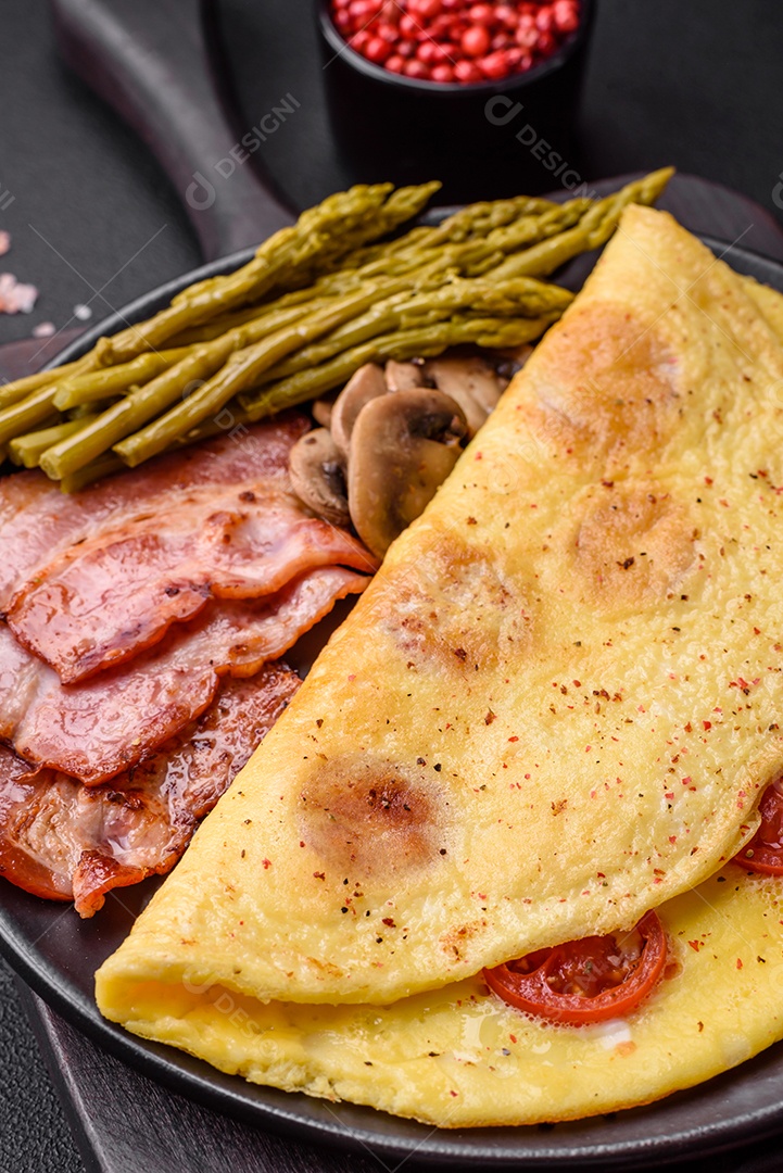 Deliciosa omelete fresca com tomate cereja, bacon, aspargos e especiarias sobre um fundo escuro de concreto