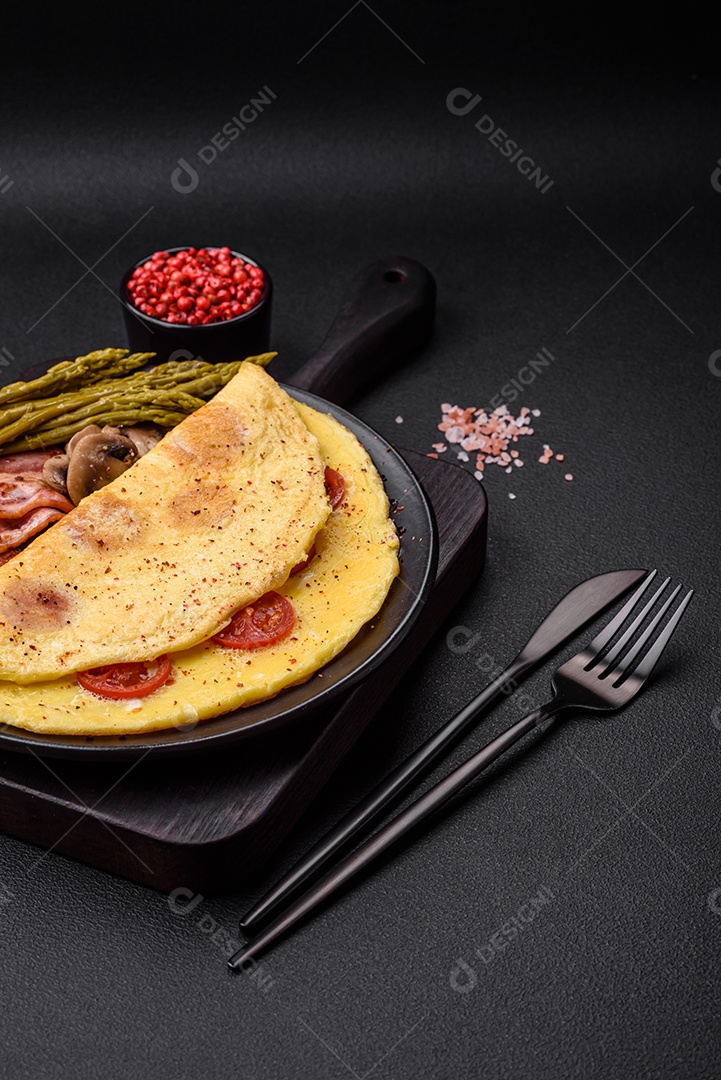 Deliciosa omelete fresca com tomate cereja, bacon, aspargos e especiarias sobre um fundo escuro de concreto