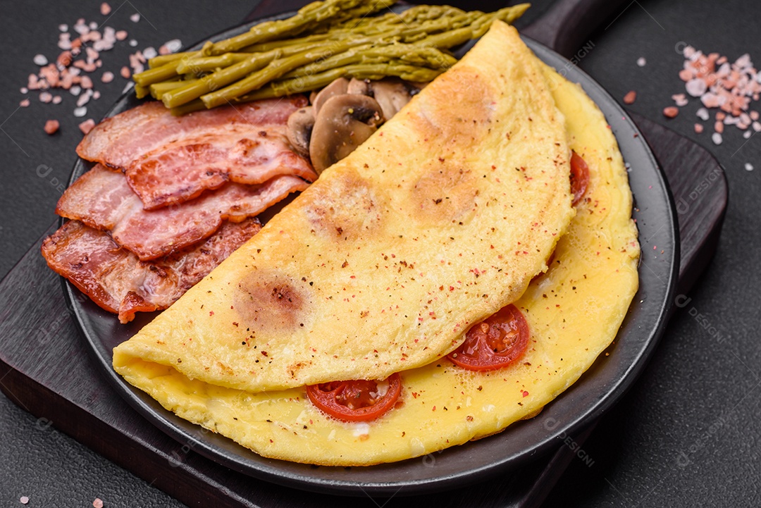 Deliciosa omelete fresca com tomate cereja, bacon, aspargos e especiarias sobre um fundo escuro de concreto