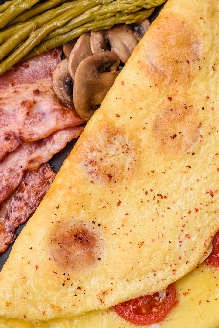 Deliciosa omelete fresca com tomate cereja, bacon, aspargos e especiarias sobre um fundo escuro de concreto