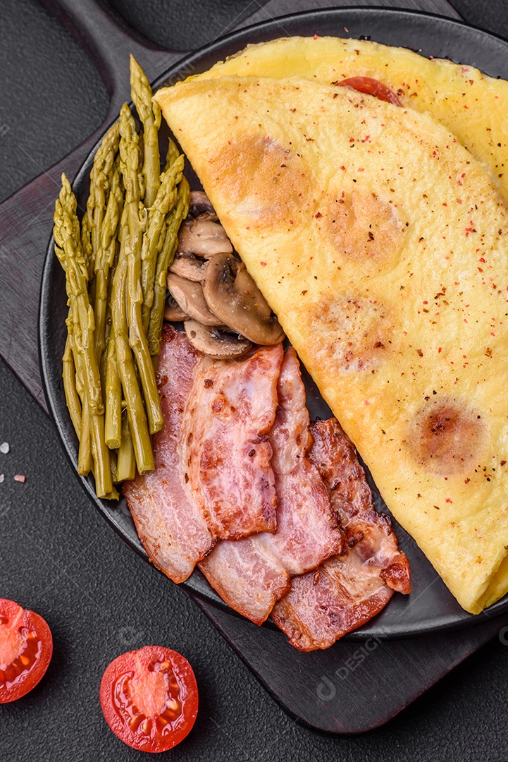 Deliciosa omelete fresca com tomate cereja, bacon, aspargos e especiarias sobre um fundo escuro de concreto
