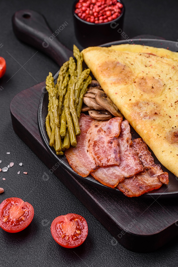 Deliciosa omelete fresca com tomate cereja, bacon, aspargos e especiarias sobre um fundo escuro de concreto